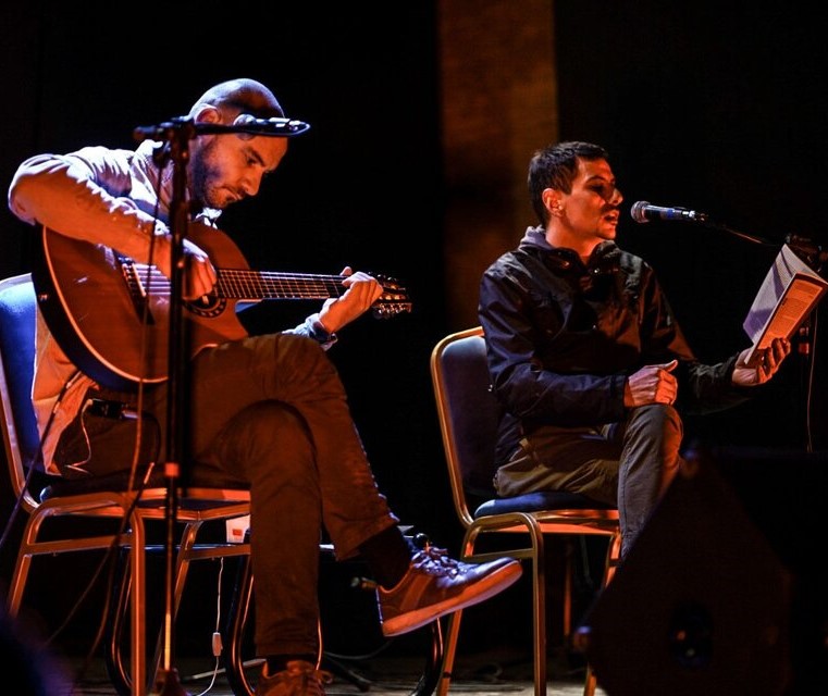 músico en guitarra y juan leyendo en escenario